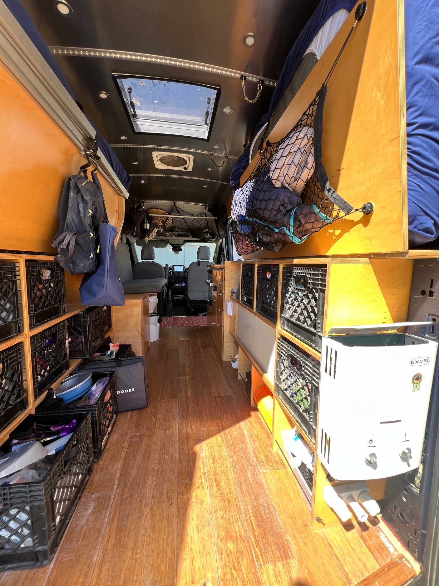 Inside this RV rental: a camper van interior with wood flooring, abundant crate storage, and overhead nets for organized travel.