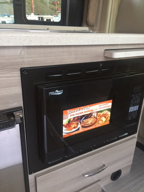 Inside an rv rental: A compact kitchen area featuring a High Pointe microwave, countertop, and wood-look cabinetry.