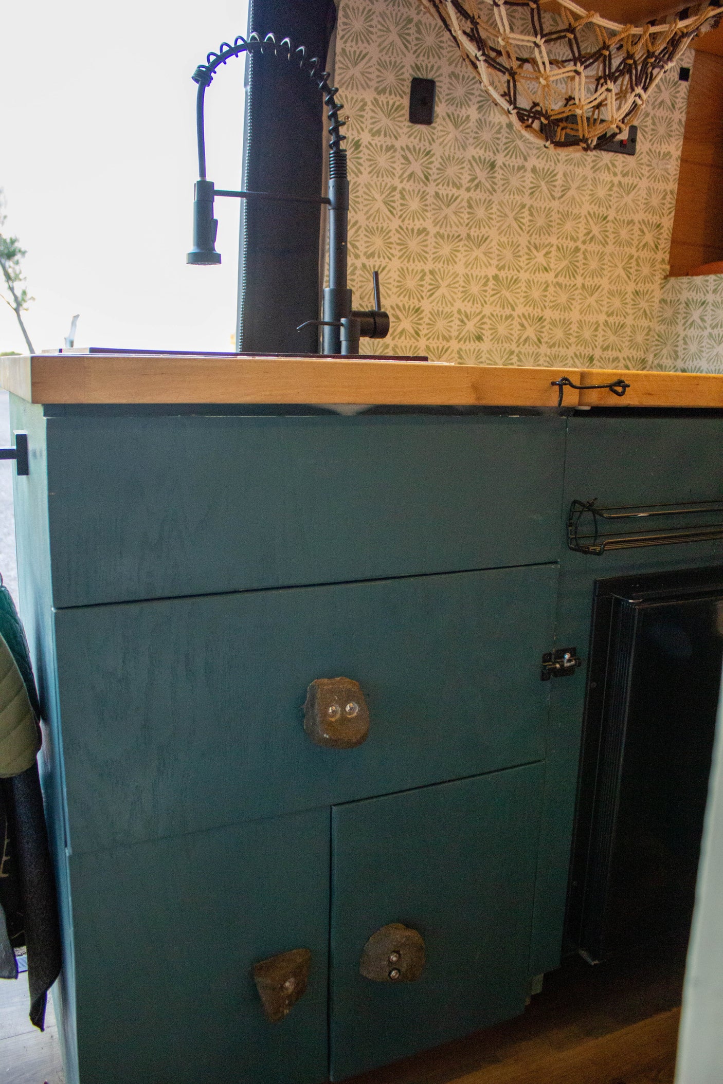 Inside an RV rental: a compact kitchen with teal cabinets, wooden counter, unique rock handles, and a modern faucet.
