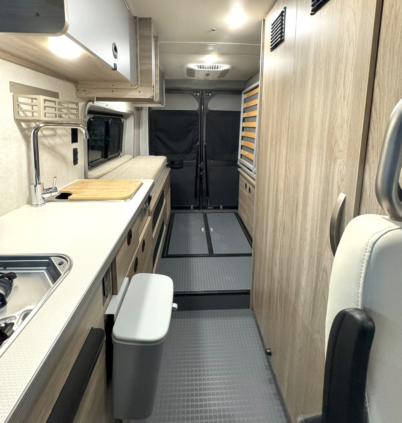 Bright rv rental interior: galley kitchen with sink, counter, storage, leading to rear doors. Features textured floor & ceiling AC.