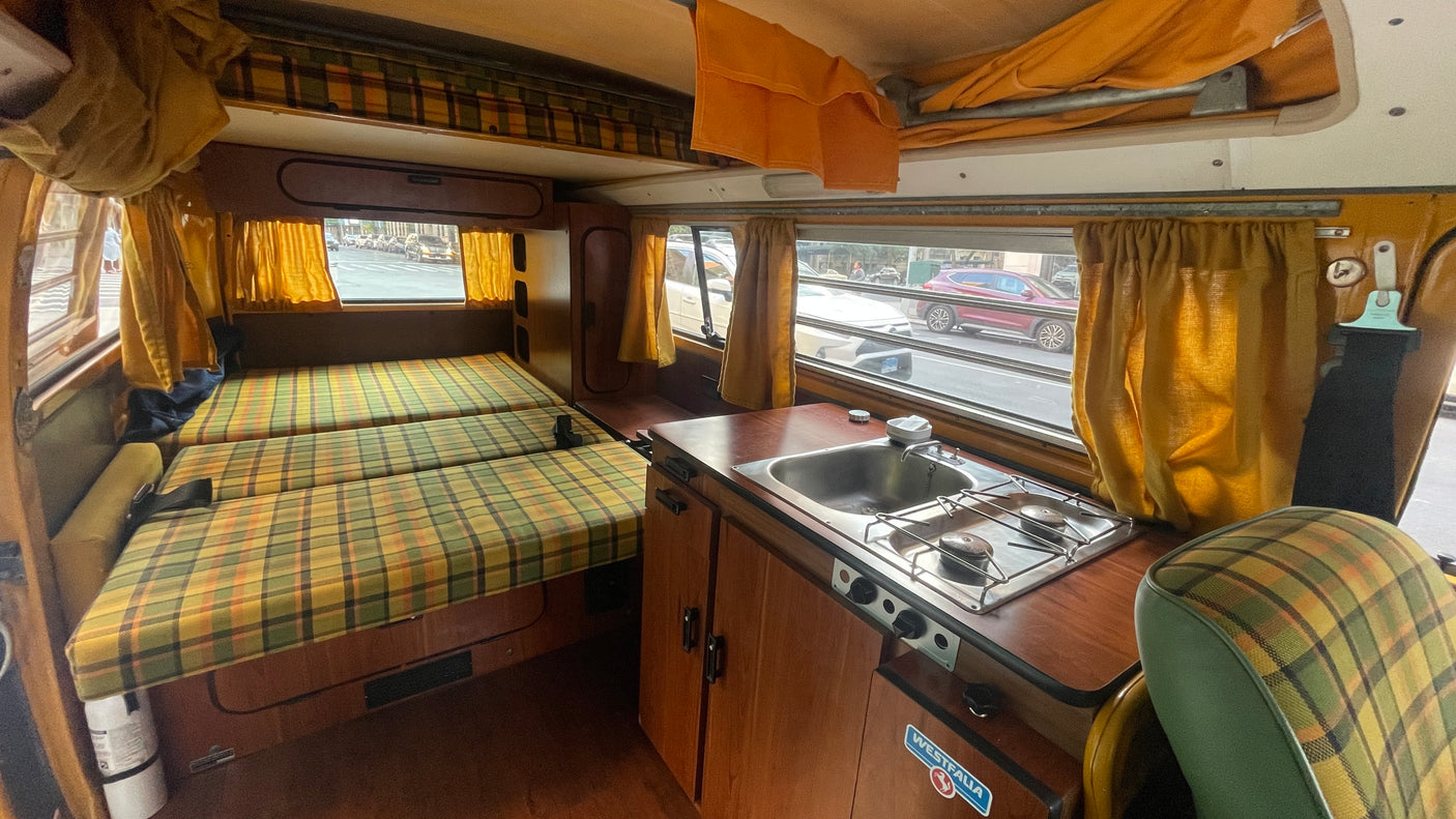 Vintage VW Westfalia camper van rv rental interior showing plaid beds, kitchen, and pop-top ceiling.