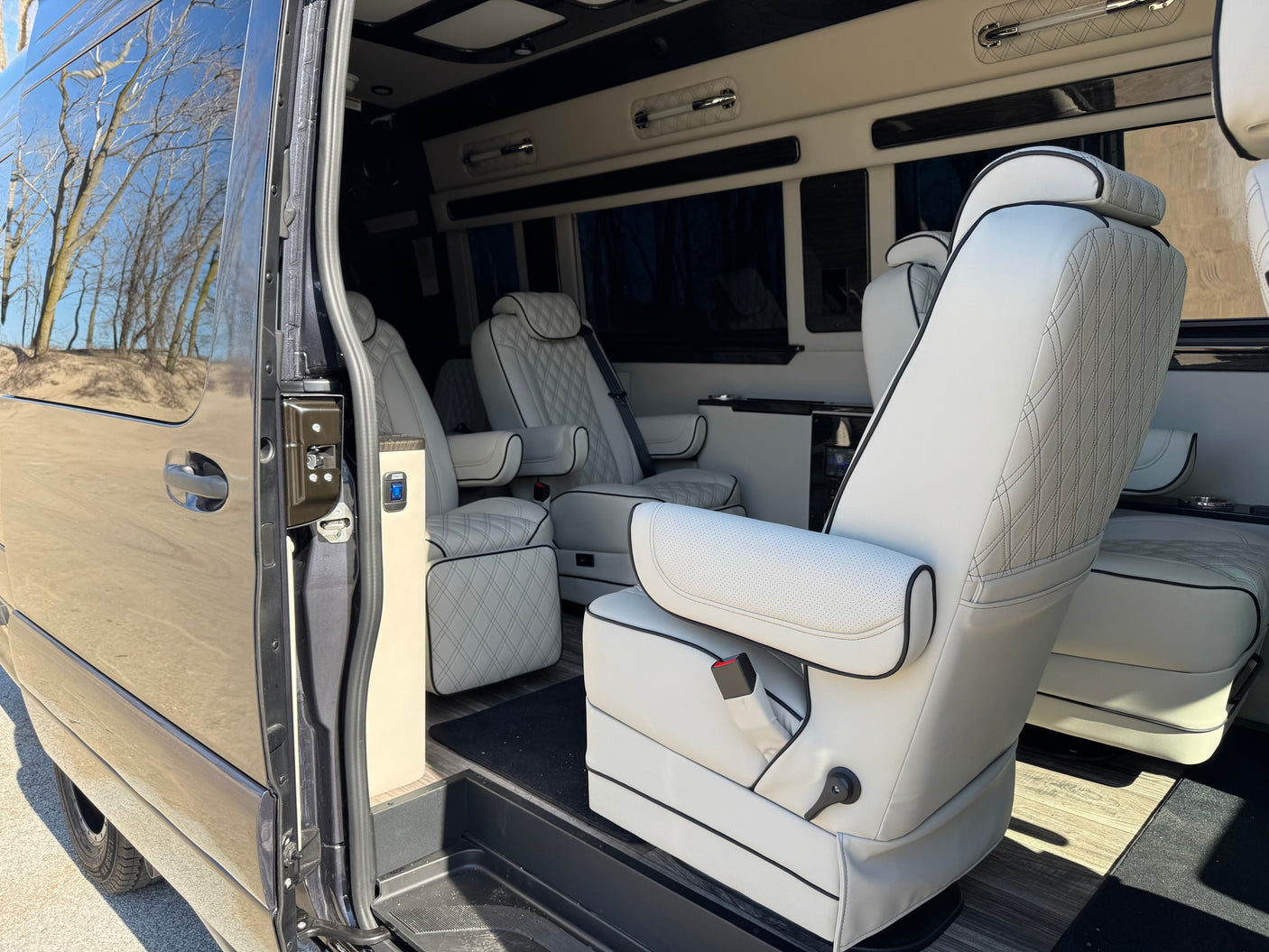 with bare trees under a blue sky.|Luxury RV rental interior: plush white captain's chairs