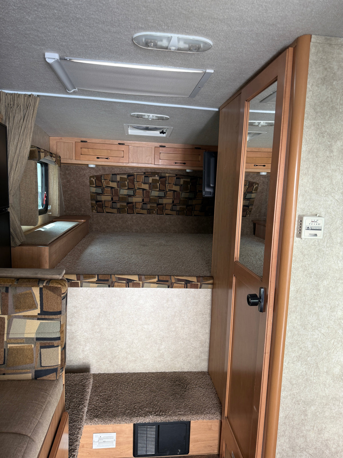 RV rental interior: elevated sleeping area with patterned headboard, overhead cabinets, and a step to the main living space. — photo 11