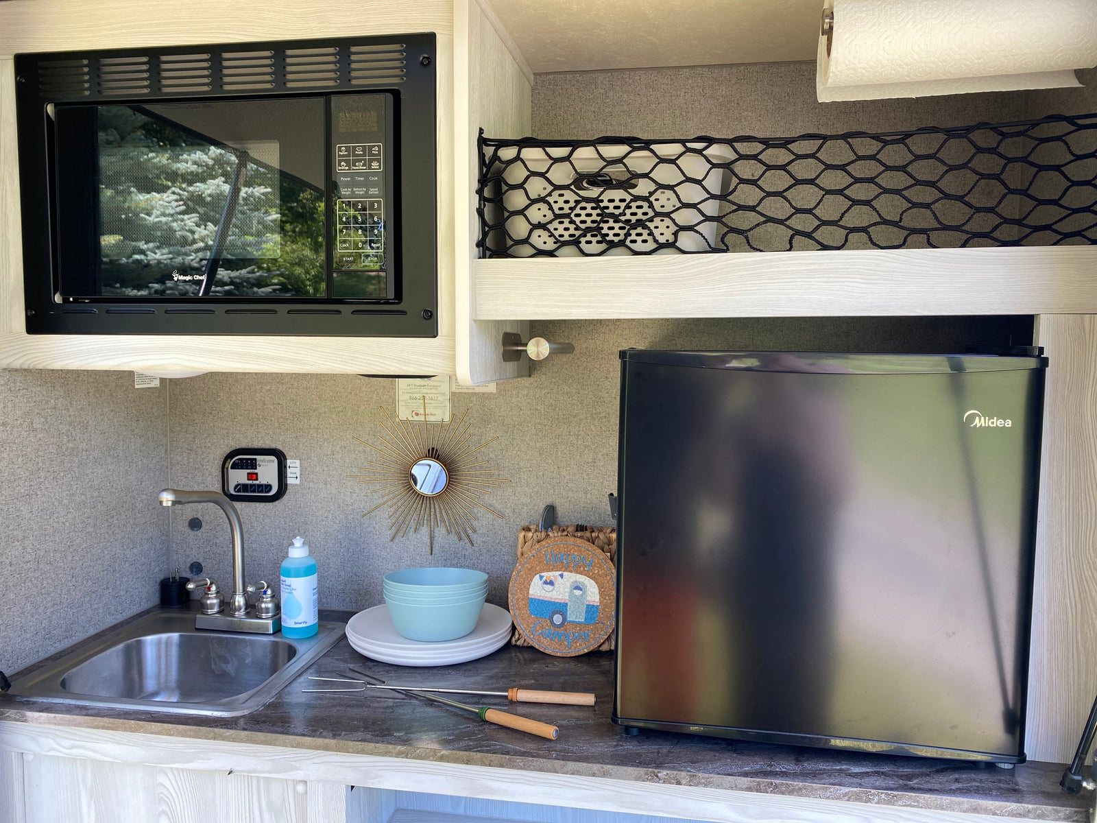 Inside an RV rental, a compact kitchenette features a microwave, sink, and refrigerator, perfect for mobile living and camping.
