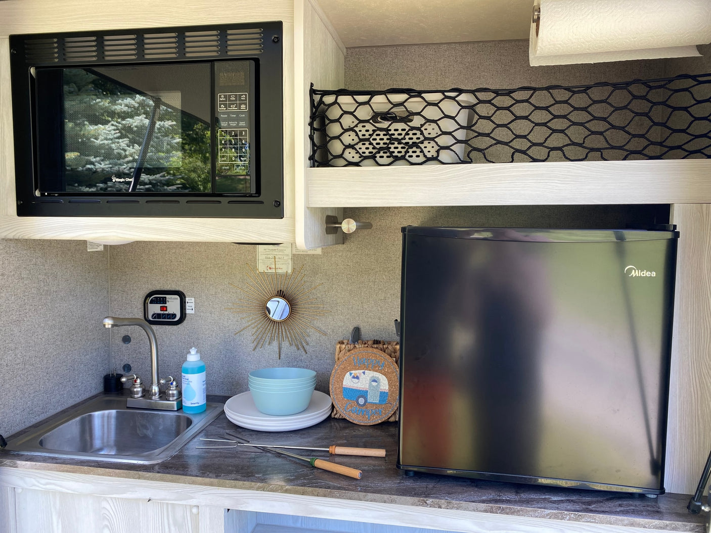 Inside an RV rental, a compact kitchenette features a microwave, sink, and refrigerator, perfect for mobile living and camping.