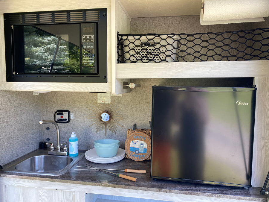 Inside an RV rental, a compact kitchenette features a microwave, sink, and refrigerator, perfect for mobile living and camping.