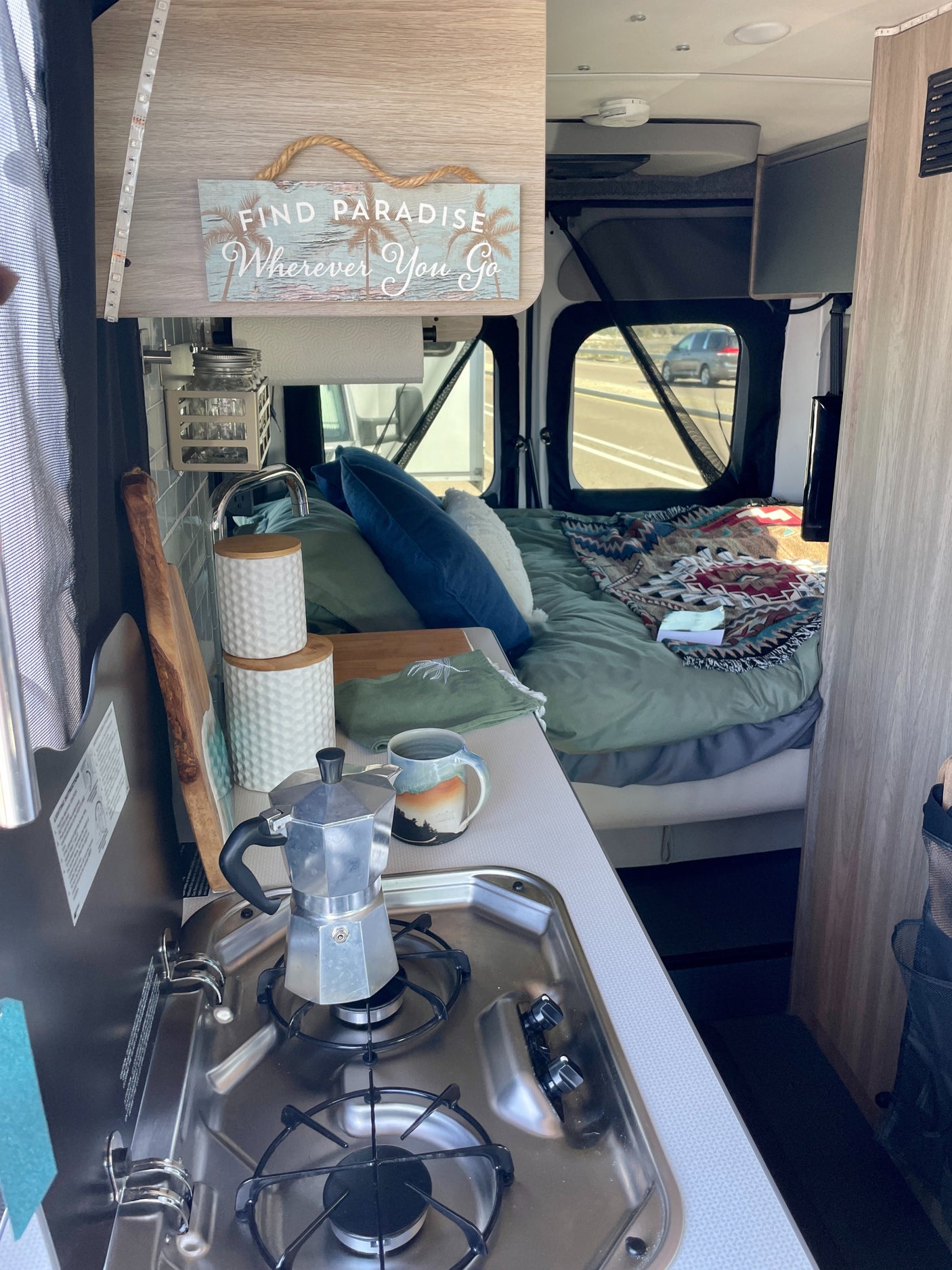 Cozy RV rental interior with kitchen, bed, and "Find Paradise" sign, ready for your next road adventure.
