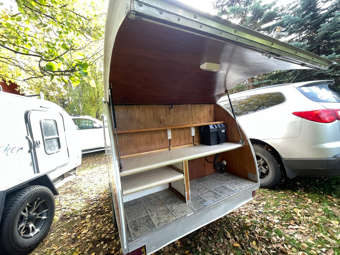 Open outdoor kitchen of an rv rental teardrop camper, featuring organized shelves, outlets, and battery power for camping.