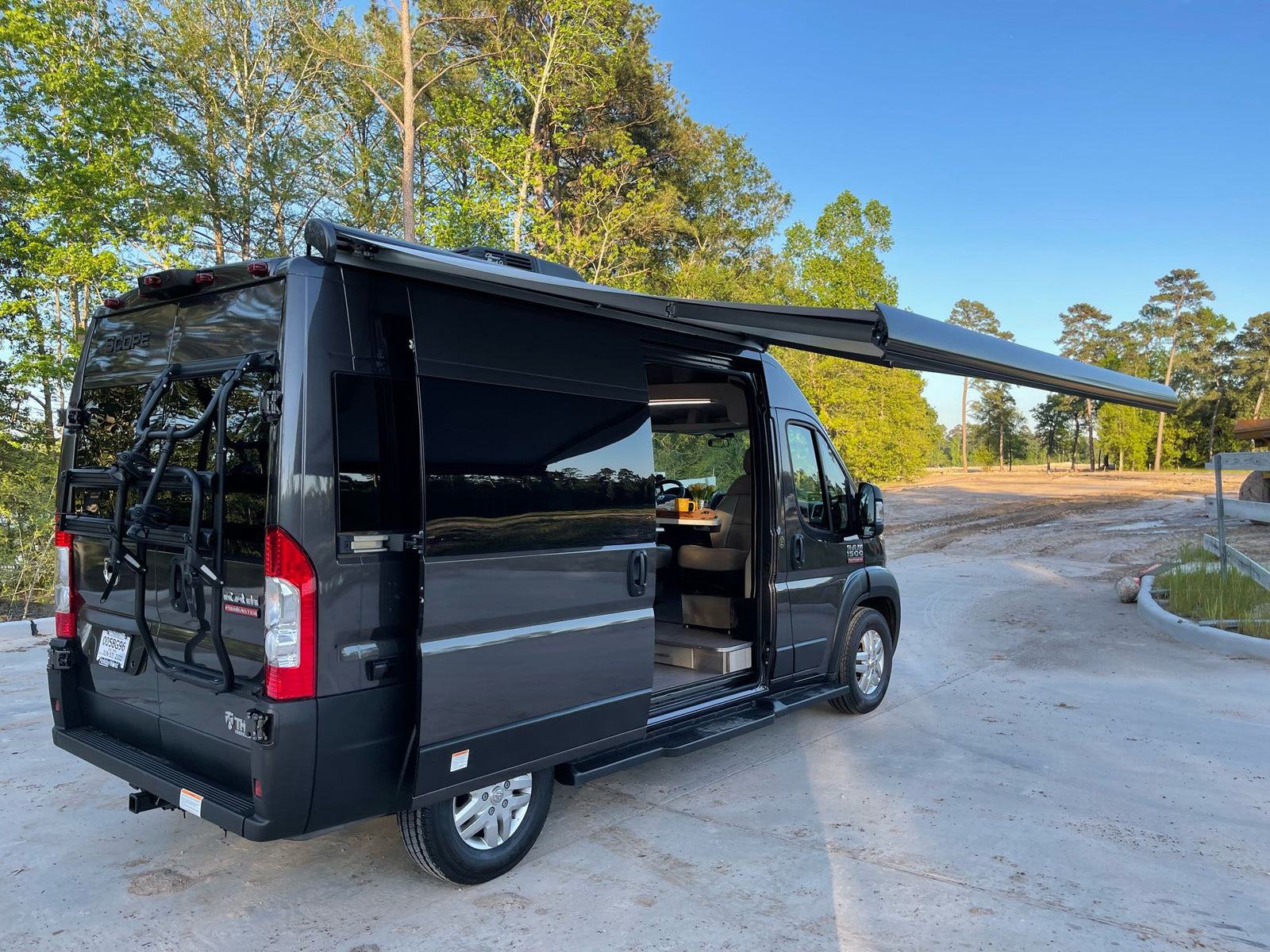 This black camper van, perfect for rv rental, features an extended awning & bike rack, parked outdoors.