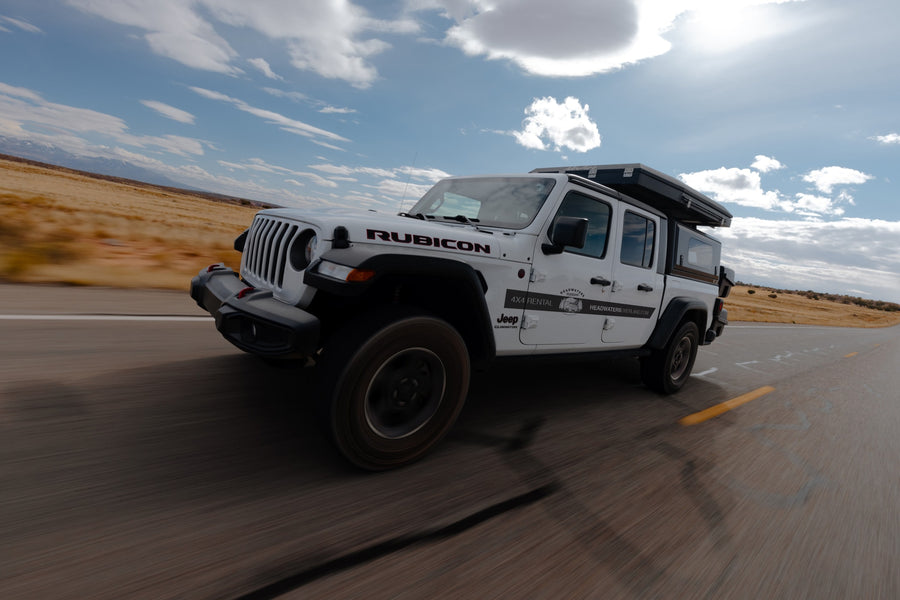 White Jeep Gladiator RV rental with rooftop tent on an open road. Ideal for adventure travel & overlanding.