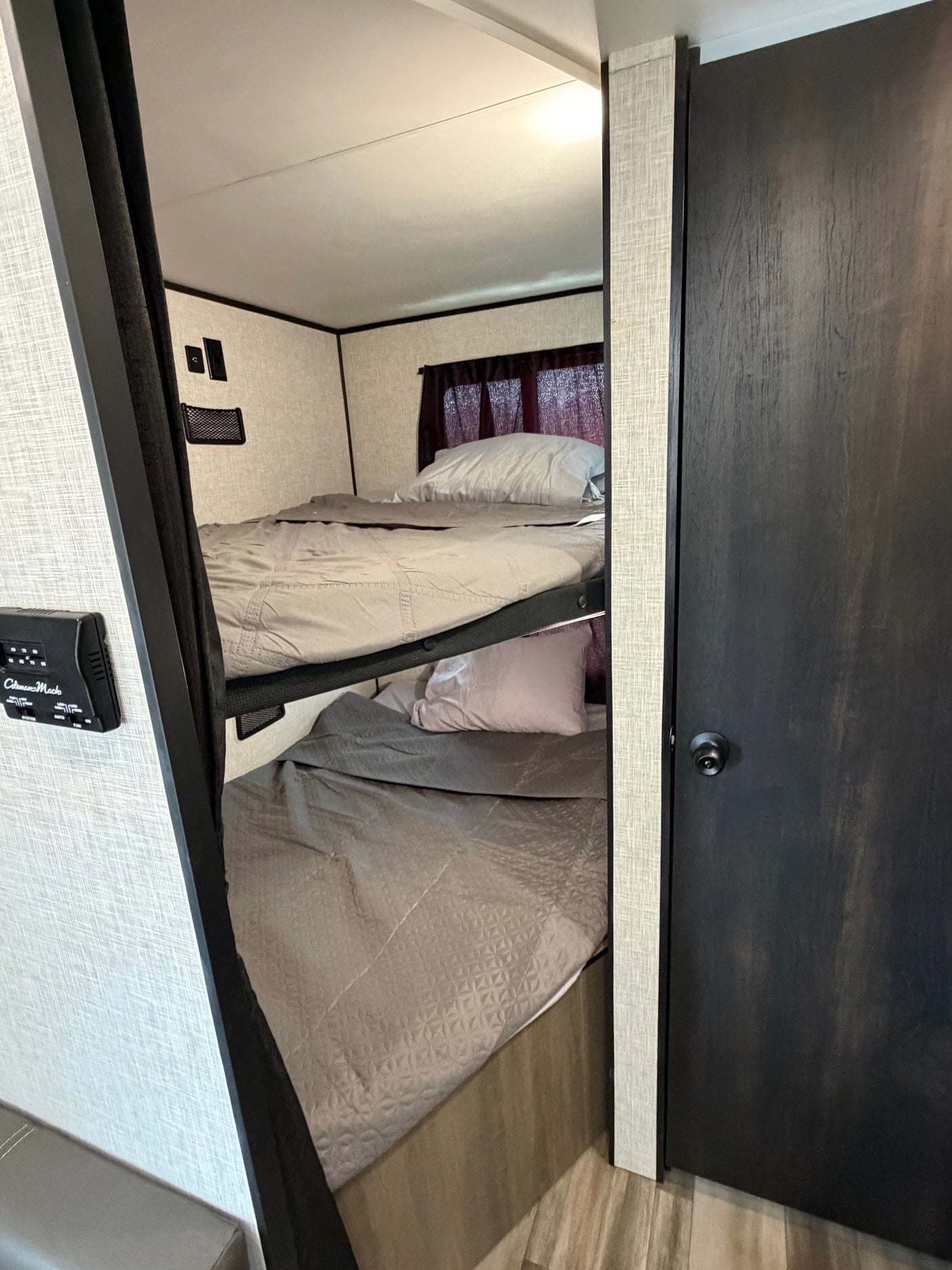Compact rv rental bunk beds with gray bedding, a control panel, and a dark door, offering cozy sleeping in an RV interior.