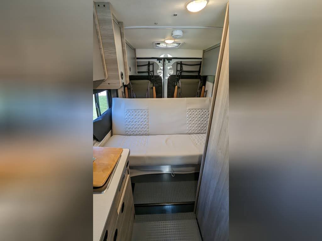 offering a view outside for your adventure.|An RV rental emerges from a natural rock tunnel. Its bright headlights illuminate the rugged passage and a mountain view.|Bright day