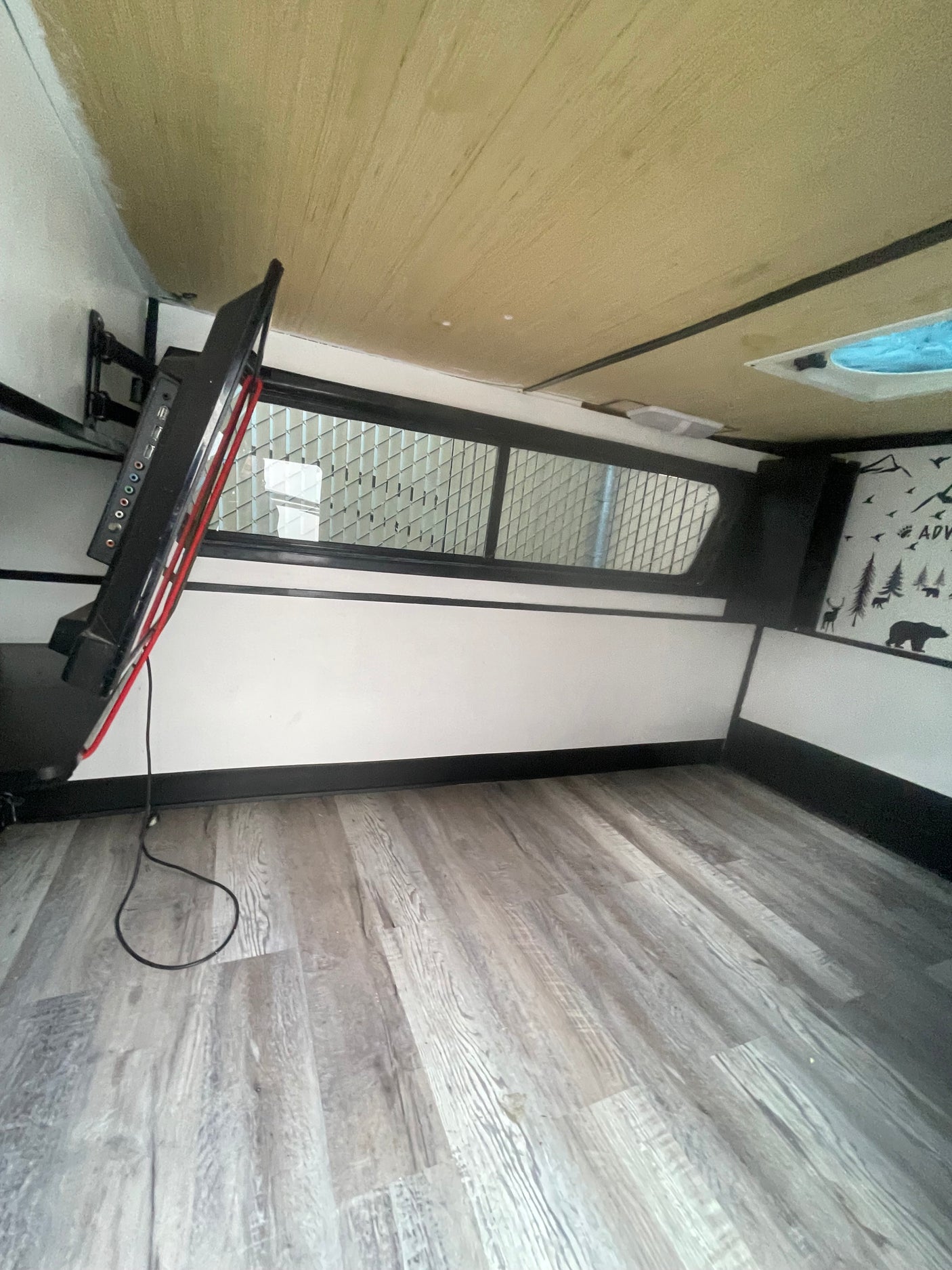 Interior of an RV rental showing a mounted TV, gridded window, wood floor, and adventure wall decals.