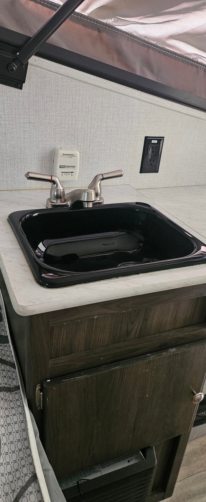 This RV rental features a compact kitchen counter with a black sink, brushed nickel faucet, and a Suburban thermostat.