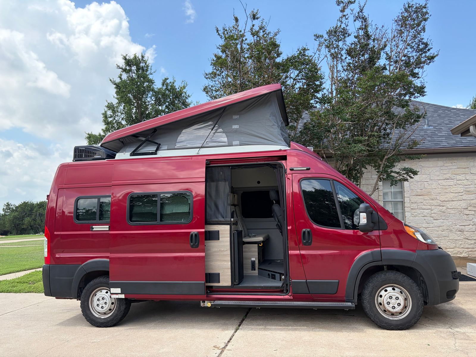 Red camper van with a pop-top roof and open side door, showing the interior. Ideal for an rv rental getaway.