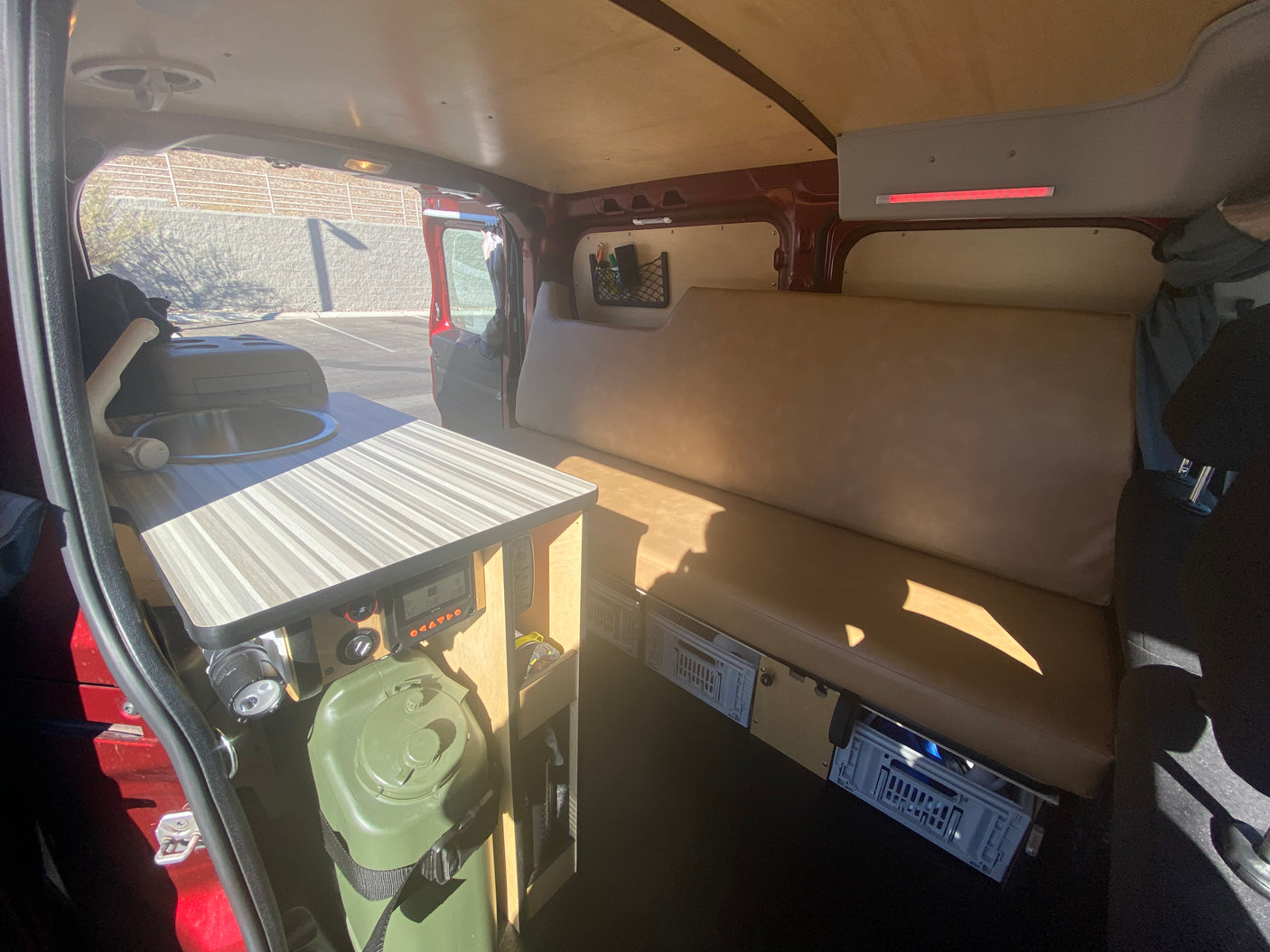 Functional camper van interior: Features a compact kitchen with sink, long bench seat, and under-seat storage, ideal for an RV rental.