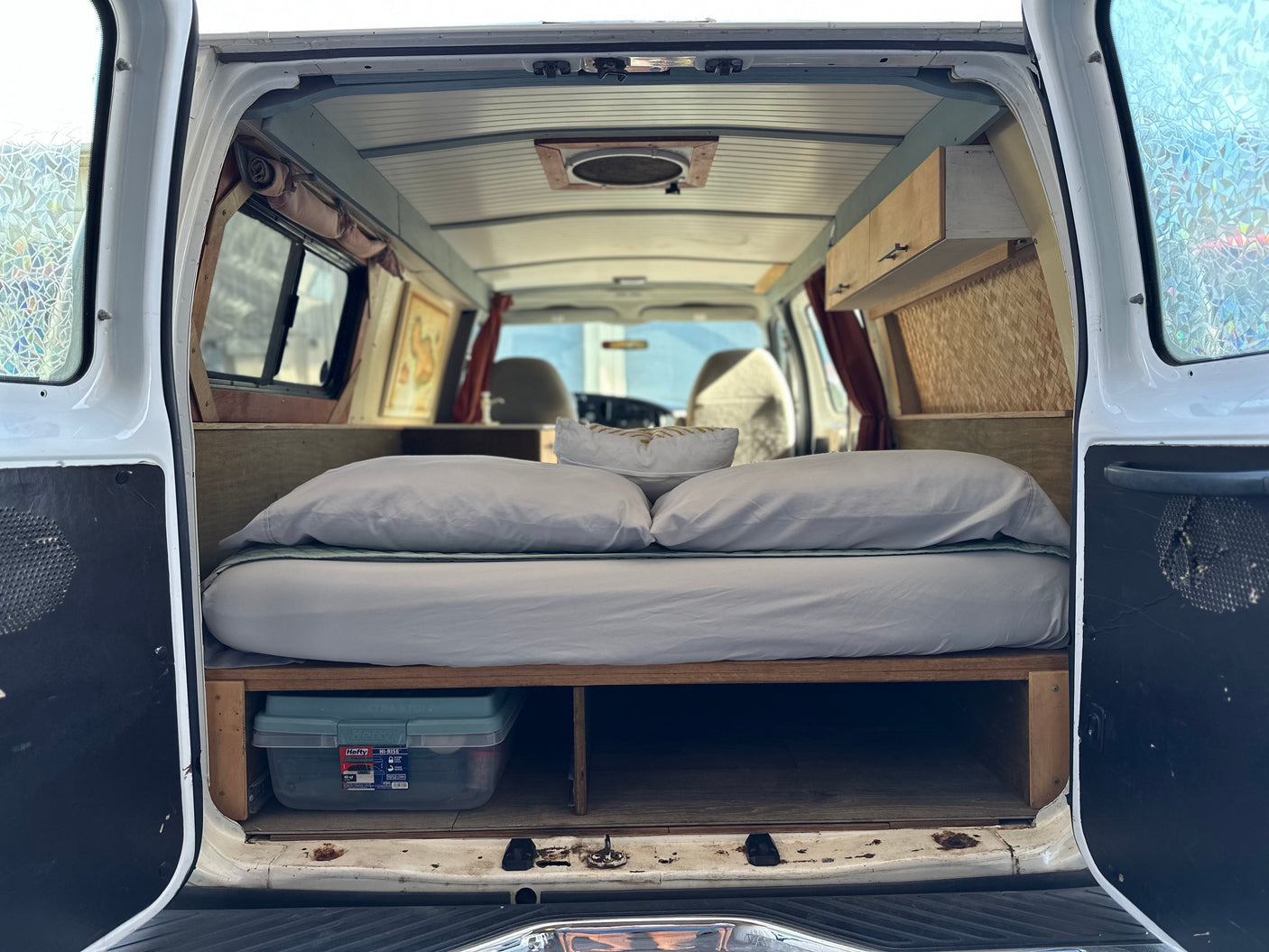 RV rental: Inside a cozy camper van conversion with a bed, under-bed storage, overhead cabinets, and a ceiling fan.