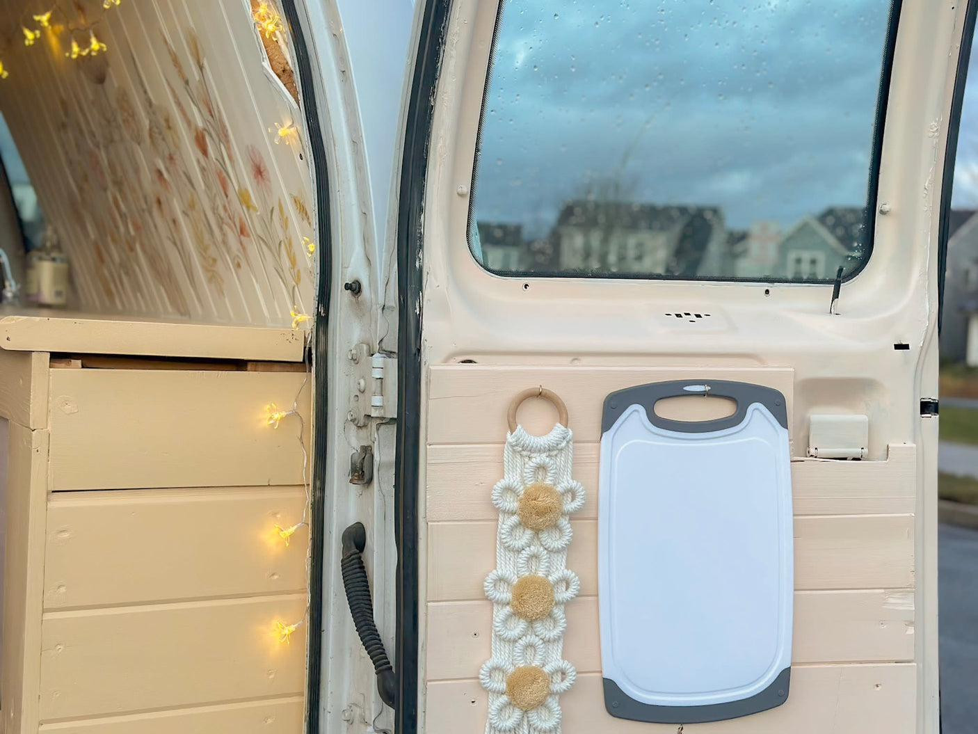 RV rental interior: organized storage with decorative lights, macrame art, and a practical cutting board mounted on the back door.