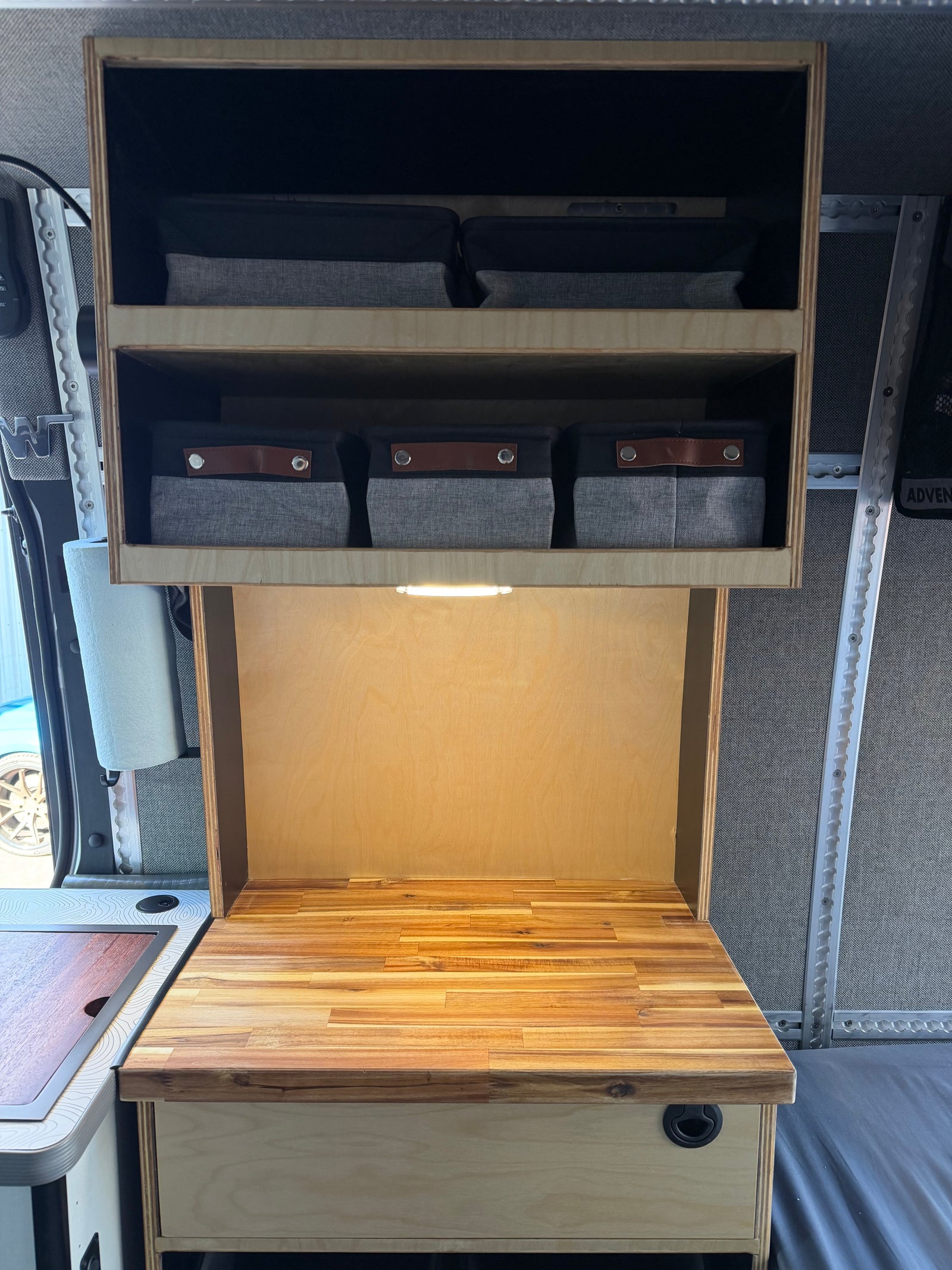 RV rental interior: Organized wooden cabinets, bright countertop lighting, and fabric storage bins in a compact camper kitchen.
