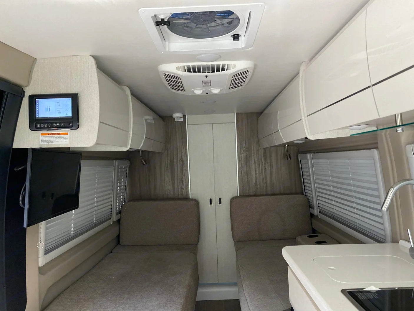 Spacious RV rental interior featuring twin beds, overhead storage, and kitchen. Ideal for comfortable road trip adventures.