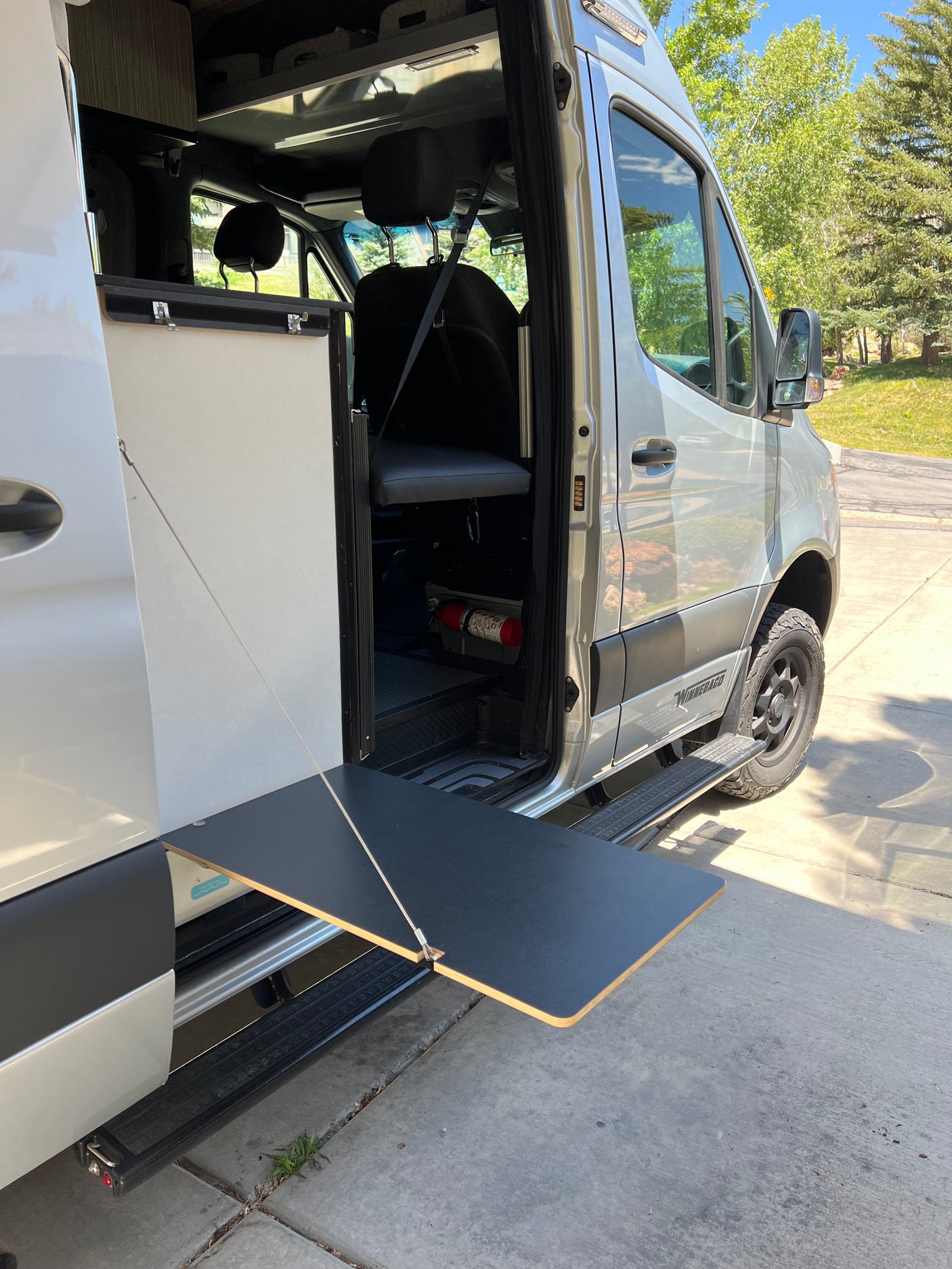 Silver camper van, ideal for rv rental adventures. Side door open, revealing interior & an extendable outdoor table.