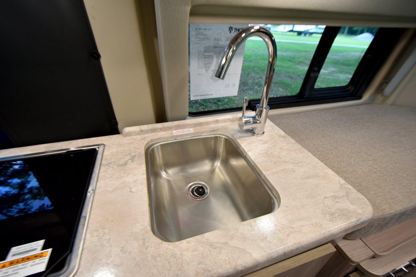 RV rental interior: A compact kitchen with a stainless steel sink, modern faucet, and light-colored countertop with cooktop. — photo 14