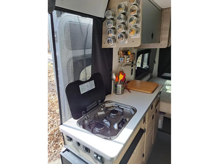 Compact RV rental kitchen with a stove, sink, spice rack, and cooking essentials. Perfect for road trip meals.