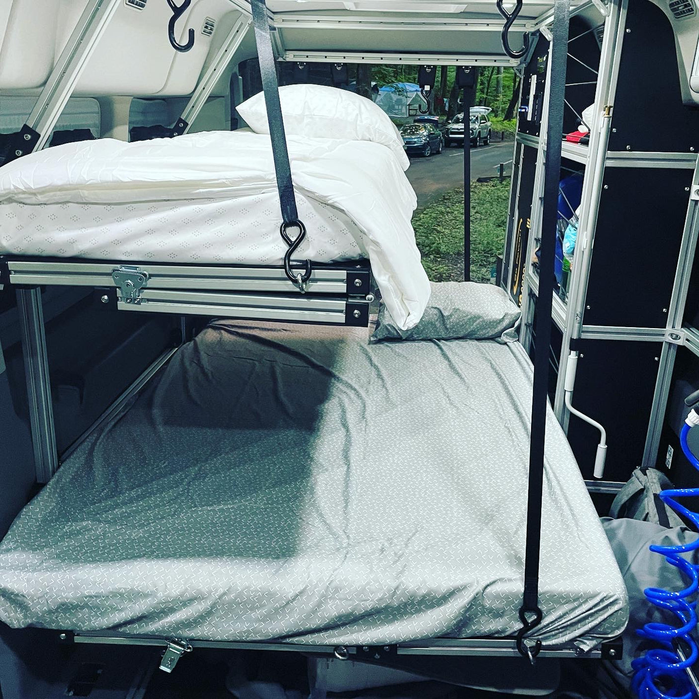 See a camper van RV rental interior with suspended white bunk beds over a grey bed, ideal for camping adventures.