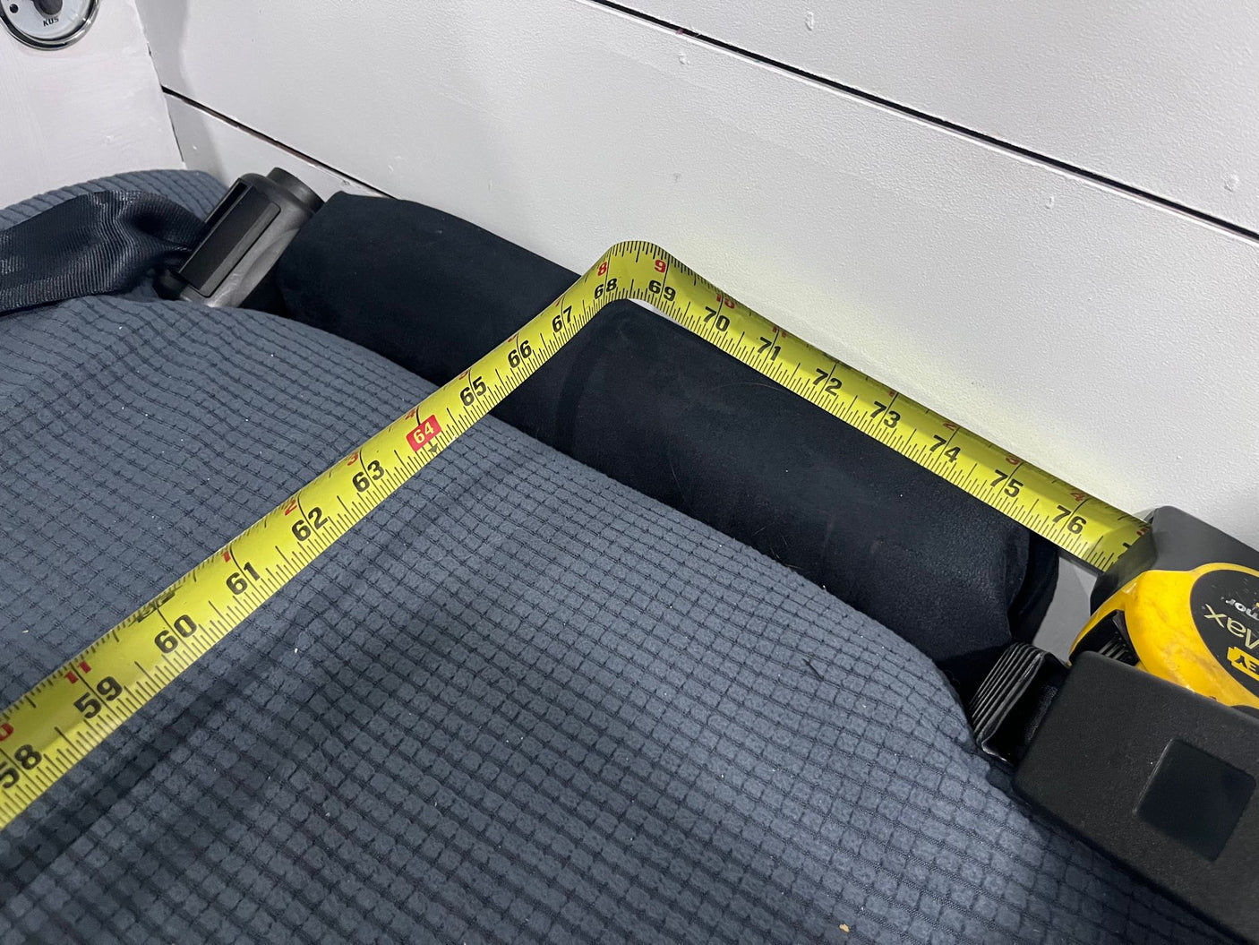 RV rental: Tape measure spanning a dark gray sleeping area, showing a length from approximately 58 to 76 inches. Practical RV space measurement.