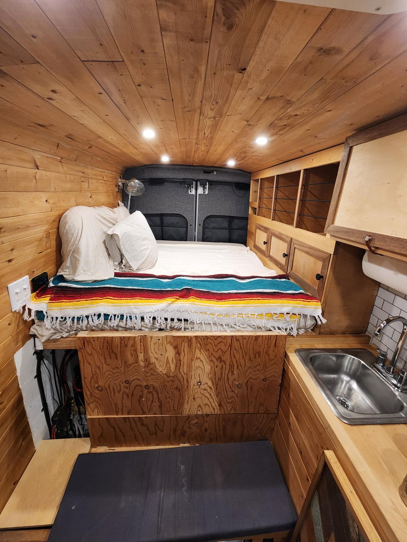 offering stunning mountain and forest views at sunset. Perfect for adventure!|Wood-paneled RV rental interior featuring a cozy bed with a colorful blanket — photo 2