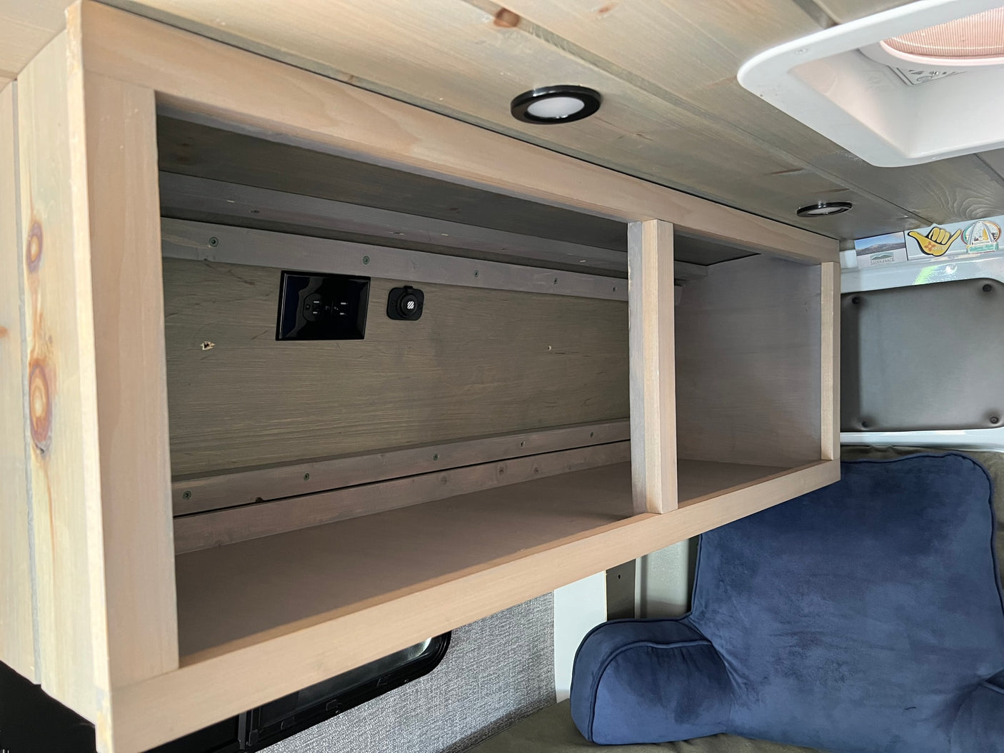 Inside this RV rental, a custom wood overhead cabinet offers convenient storage with AC and USB outlets, brightened by ceiling lights.