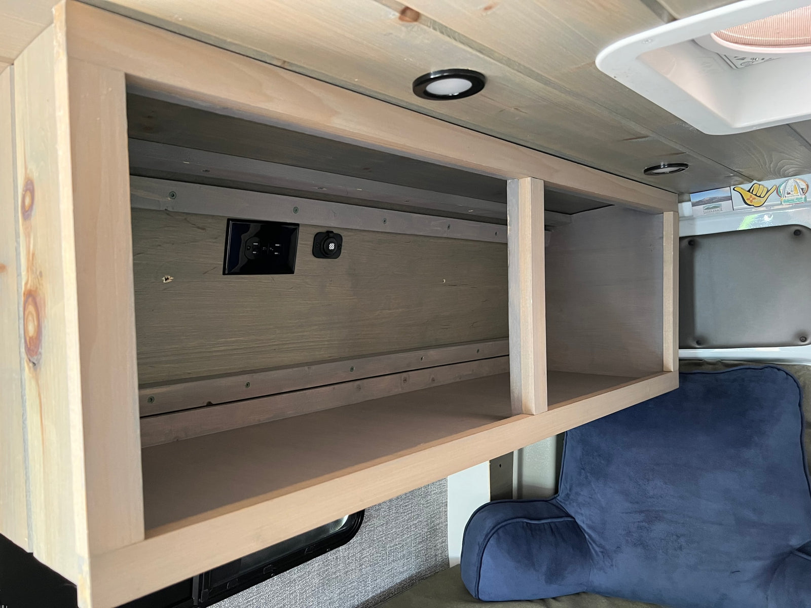 Inside this RV rental, a custom wood overhead cabinet offers convenient storage with AC and USB outlets, brightened by ceiling lights.