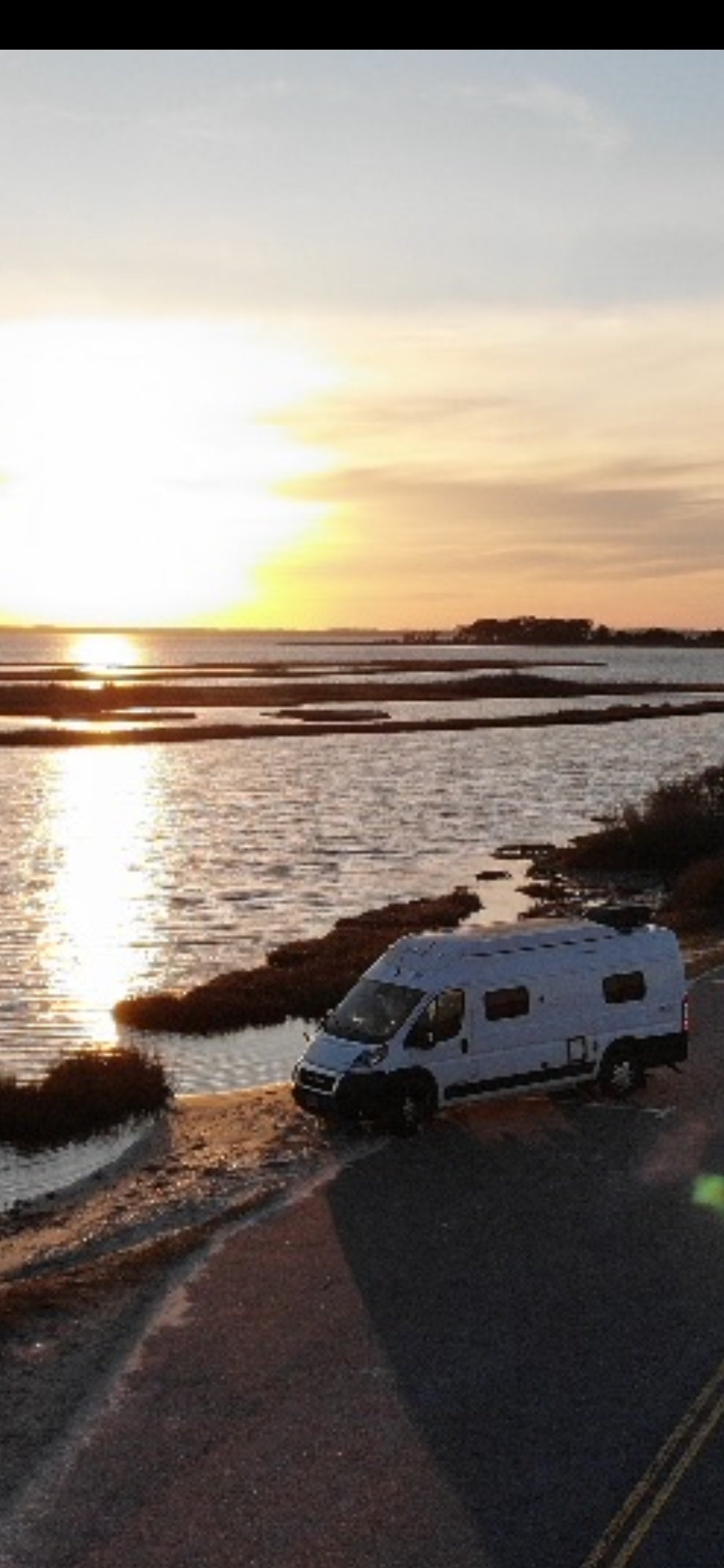 White rv rental parked beside a tranquil bay, bathed in golden sunset light. Perfect for scenic road trips.