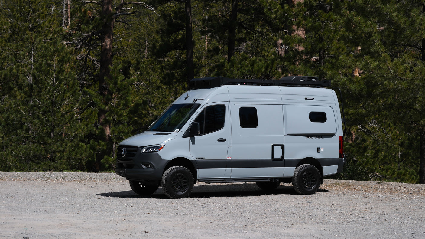Sleek gray Mercedes-Benz Sprinter RV rental parked on a forest dirt road, perfect for outdoor adventure & exploration.