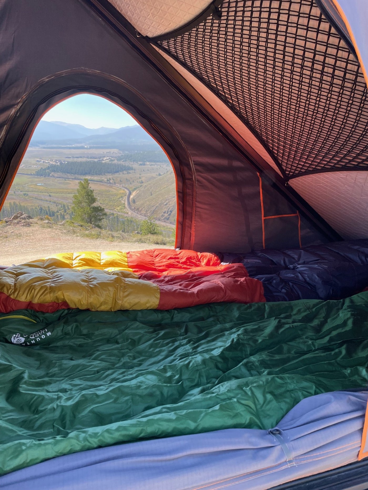 Cozy tent bed with vibrant sleeping bags looking out at a stunning valley view. RV rental adventure! — photo 7