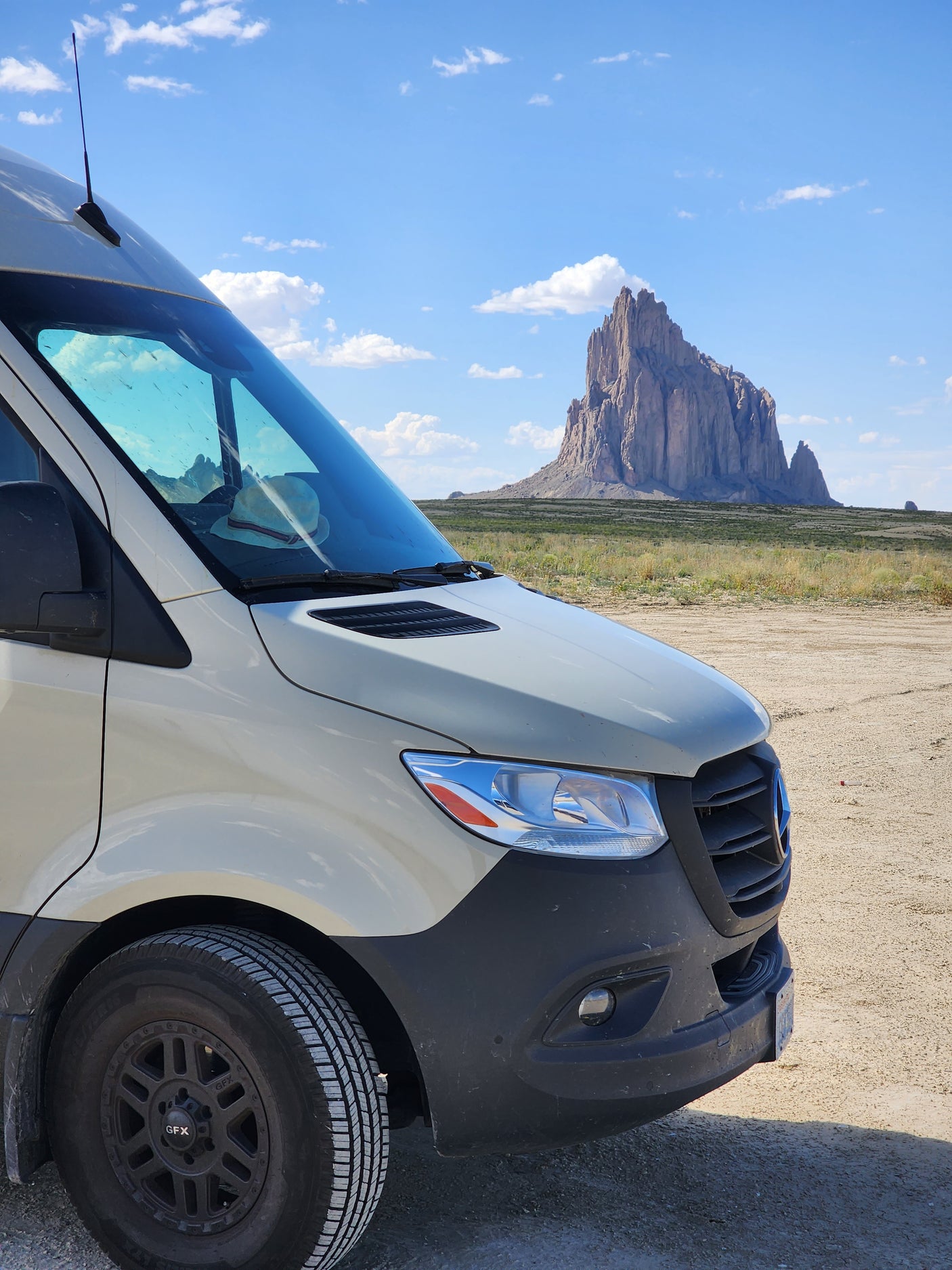 Explore with an RV rental! A camper van on a desert road, majestic mountains in the background under a vast blue sky.