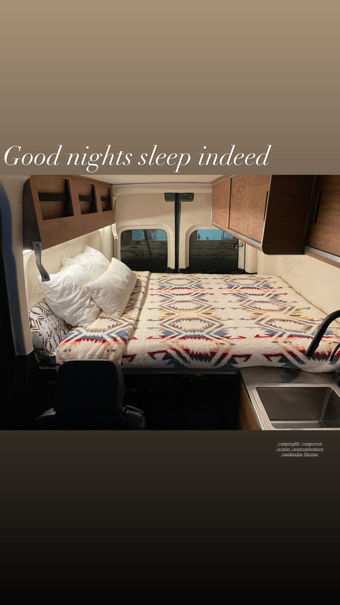 Cozy RV rental interior with a comfy bed, sink, & wood cabinets. Perfect for restful van life adventures!