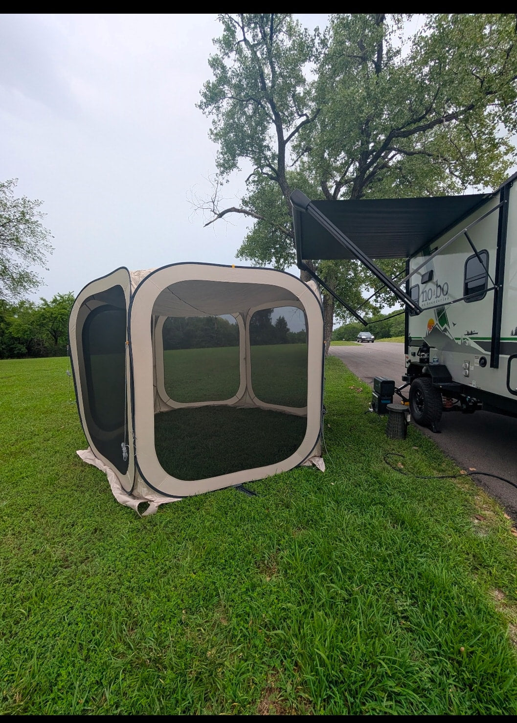 Camping with an RV rental: A screen tent is pitched beside a travel trailer with an extended awning on green grass.