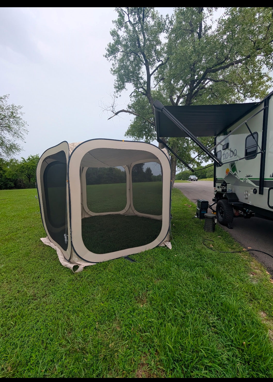 Camping with an RV rental: A screen tent is pitched beside a travel trailer with an extended awning on green grass.