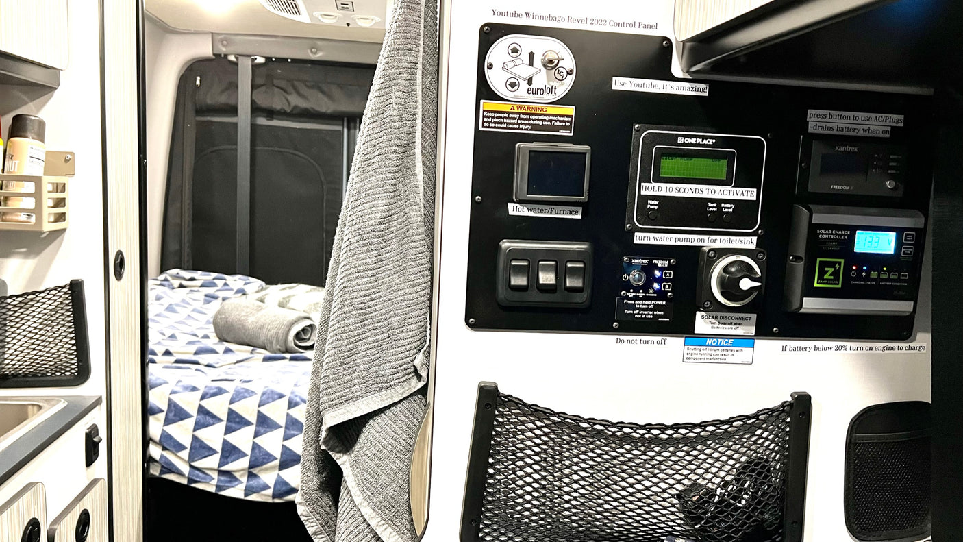 RV rental interior: A camper van's control panel, showing switches and displays for heating, water, and solar charge, beside a cozy bed.