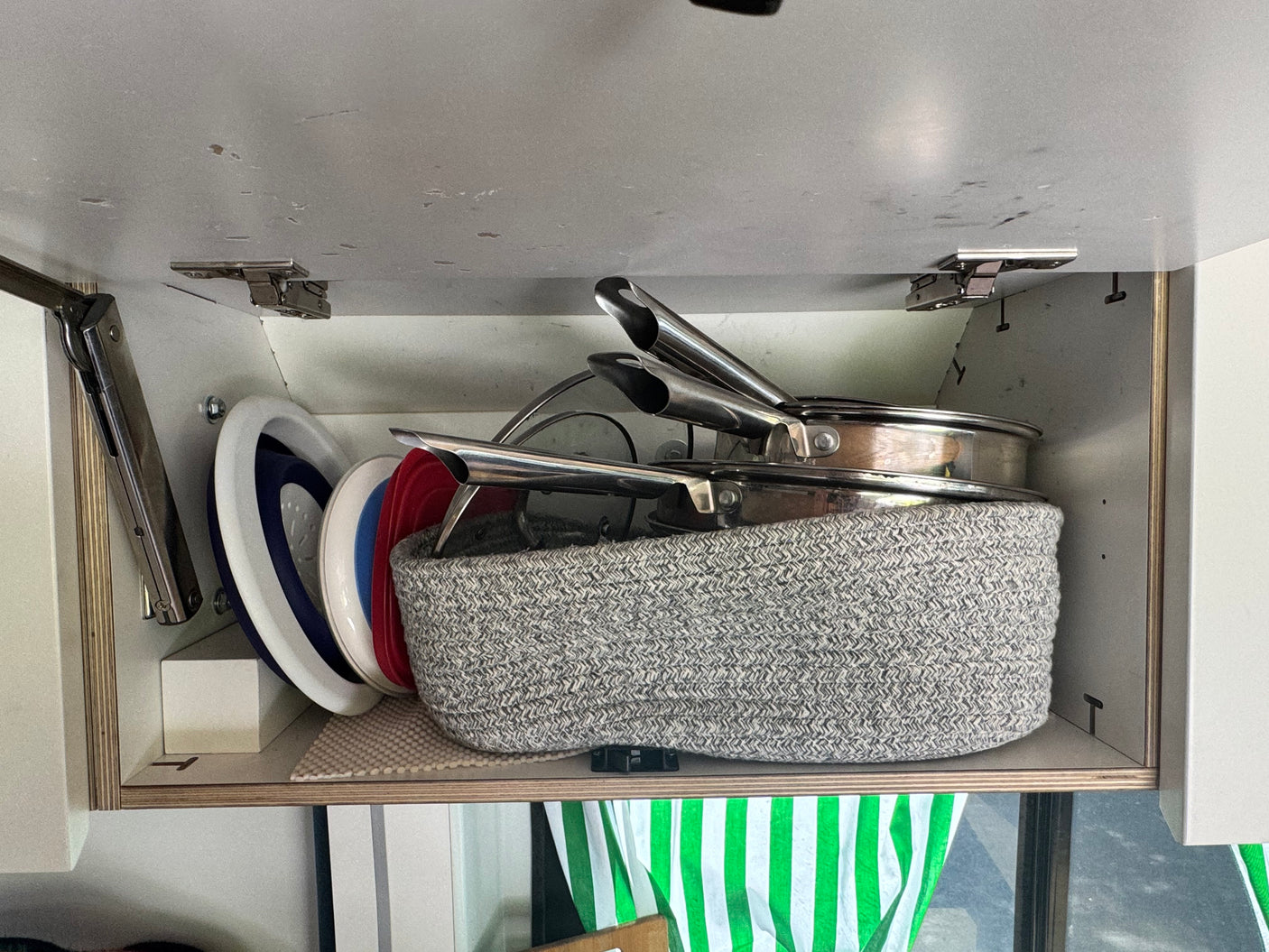 Organized kitchen essentials in an upper cabinet of an rv rental, featuring stacked pans, lids, and collapsible dishes.