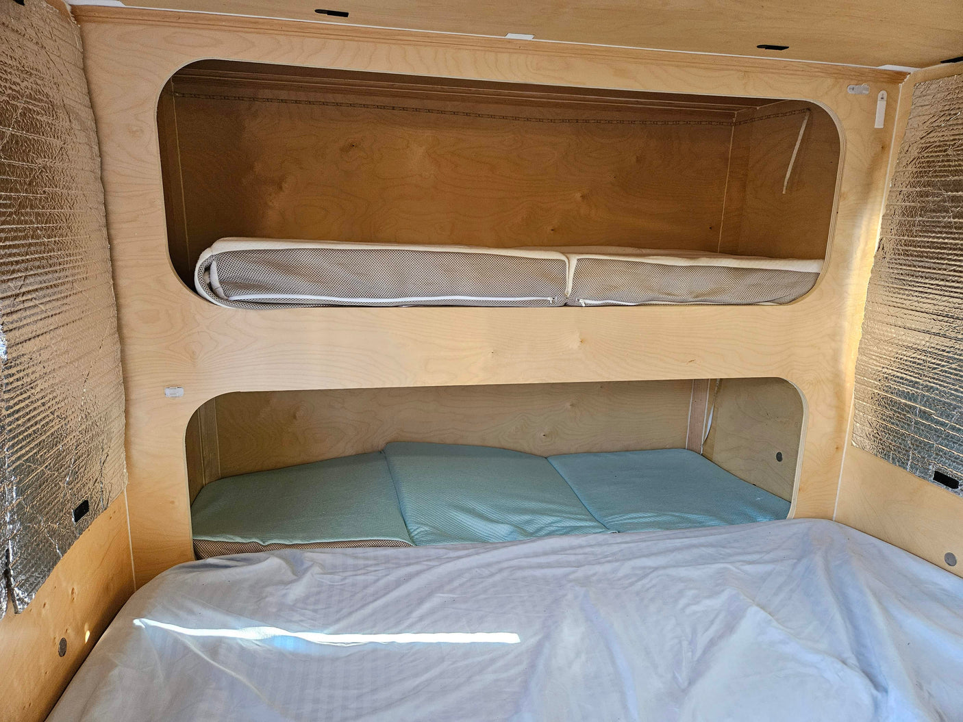 Cozy rv rental interior with light wood bunk beds (top mesh, bottom blue mattress) & insulated walls.