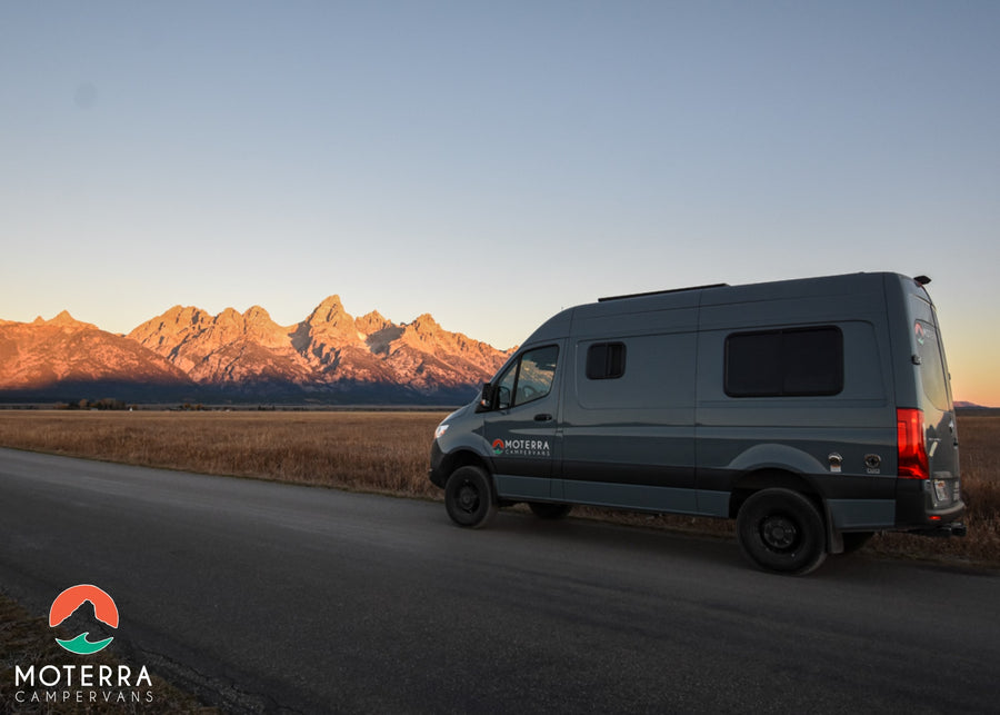 Gray RV rental campervan on a road with golden mountains at sunrise. Ideal for scenic adventure travel.