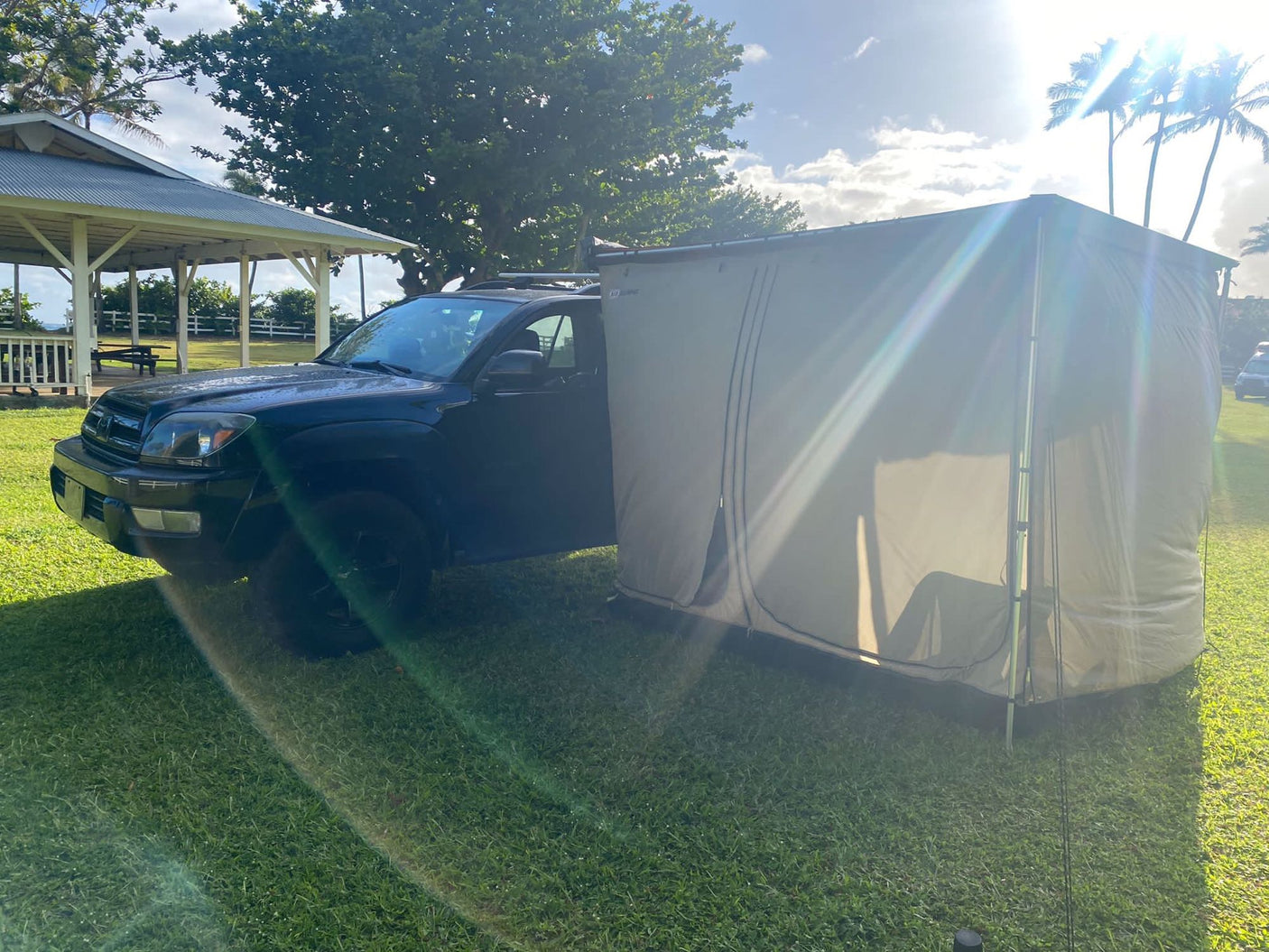 RV rental setup: Dark SUV with a large, beige privacy tent attached, perfect for camping and overlanding trips.
