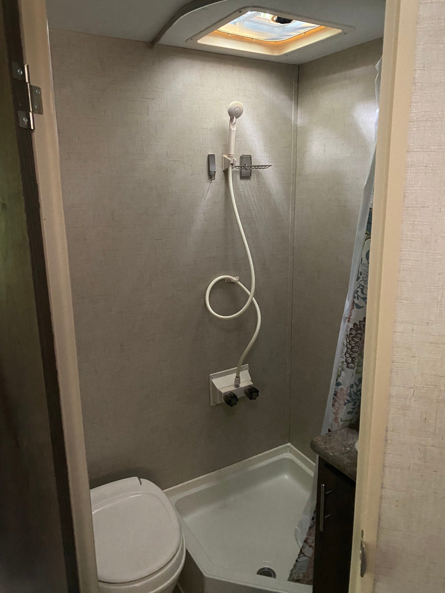 Inside an RV rental: compact bathroom with a functional shower, handheld showerhead, and toilet.