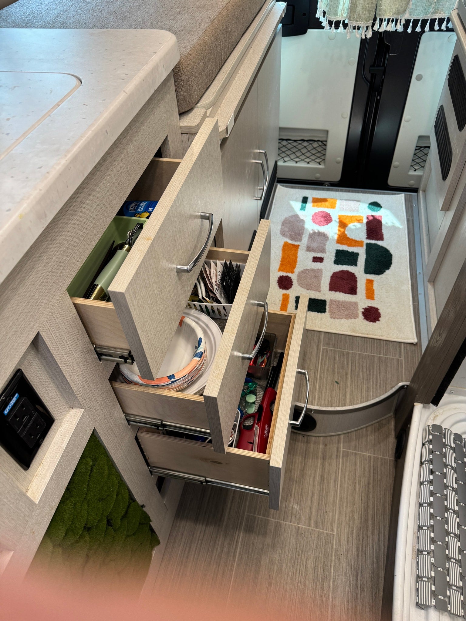 RV rental interior: three open kitchen drawers reveal organized storage for plates, tea, and supplies in a compact space.