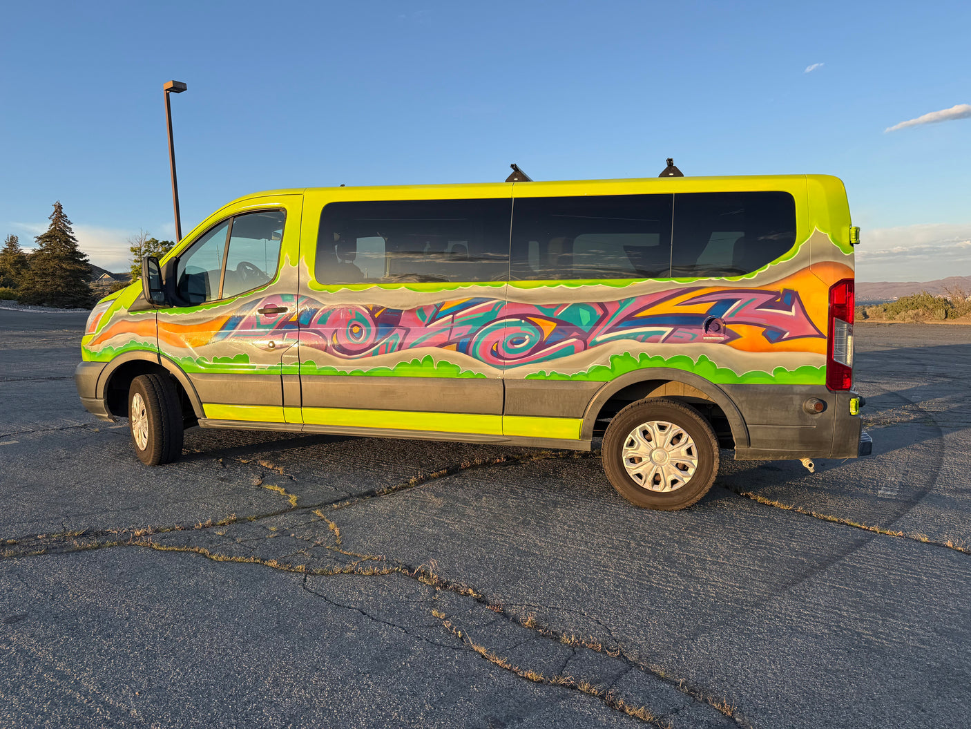 Vibrant lime-green graffiti RV rental van, ready for adventure, parked on cracked asphalt under a clear blue sky.