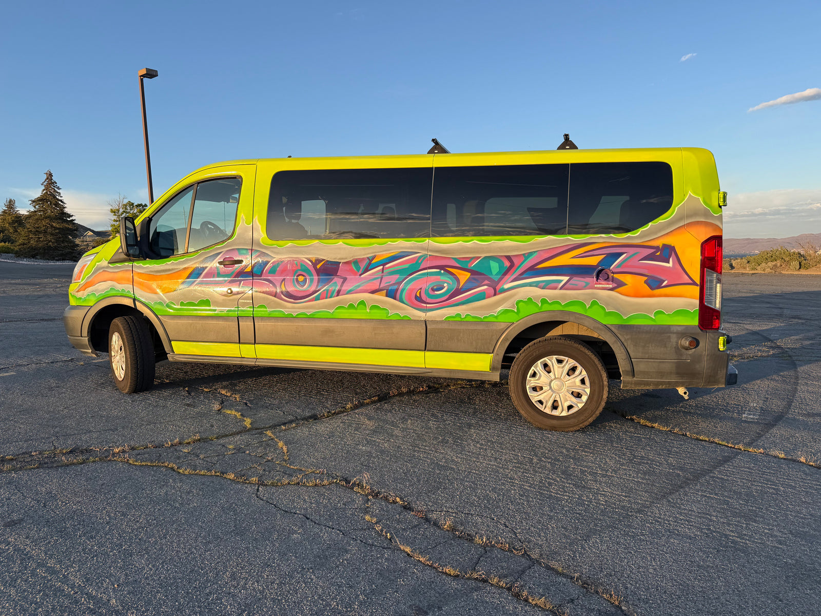 Vibrant lime-green graffiti RV rental van, ready for adventure, parked on cracked asphalt under a clear blue sky.