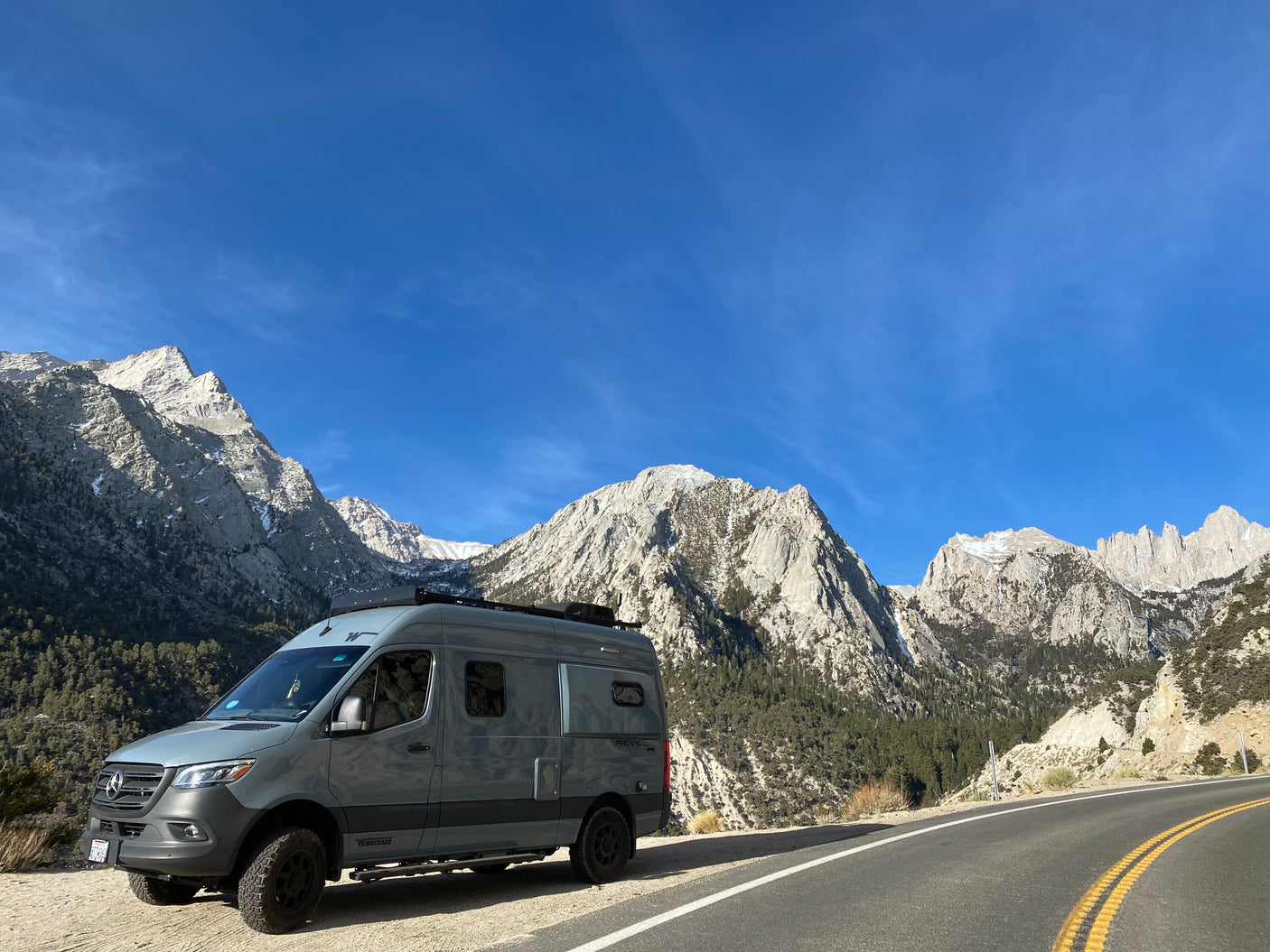 Explore majestic mountains with this Winnebago Revel RV rental van parked roadside on a sunny day.
