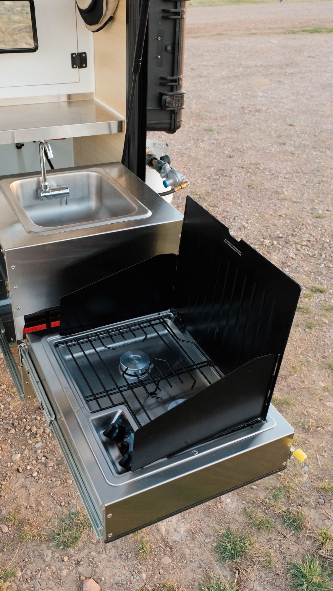 ideal for outdoor adventures in nature.|Experience an RV rental adventure! A rugged off-road camper trailer sits silhouetted against a golden sunset in a natural landscape.|This rugged Boreas XT off-road camper trailer with an open door showing its interior is perfect for an RV rental adventure.|RV rental outdoor kitchen features a pull-out stainless steel sink and gas stove with wind guards for campsite cooking.|Explore with this Boreas XT overland trailer for your next RV rental adventure. Ready for off